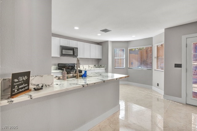 kitchen featuring light stone countertops, white cabinetry, stove, and kitchen peninsula