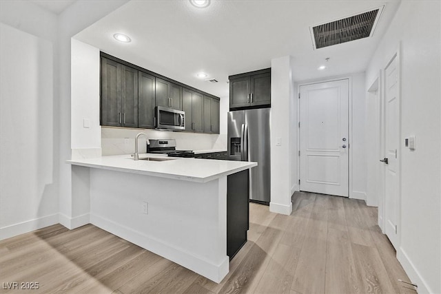 kitchen with light hardwood / wood-style floors, stainless steel appliances, kitchen peninsula, and sink