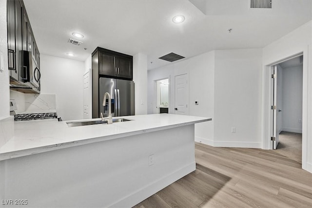 kitchen featuring tasteful backsplash, stainless steel appliances, kitchen peninsula, and light wood-type flooring