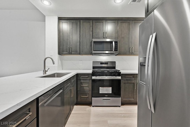 kitchen with sink, appliances with stainless steel finishes, light stone counters, dark brown cabinetry, and light wood-type flooring