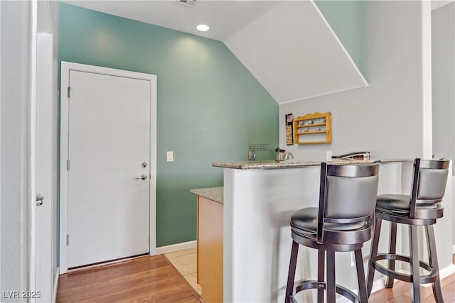 kitchen with a breakfast bar area, light stone counters, vaulted ceiling, light wood-type flooring, and kitchen peninsula