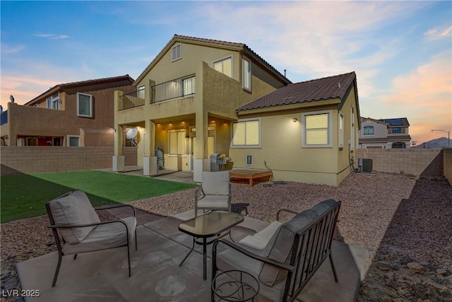 back house at dusk featuring cooling unit, a yard, a patio area, and a balcony