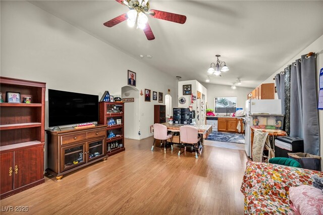 living room featuring ceiling fan with notable chandelier, vaulted ceiling, and light wood-type flooring