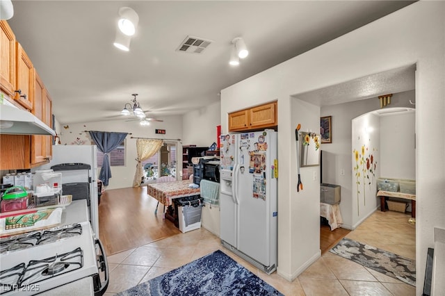 kitchen featuring gas stove, white refrigerator with ice dispenser, light tile patterned floors, and ceiling fan