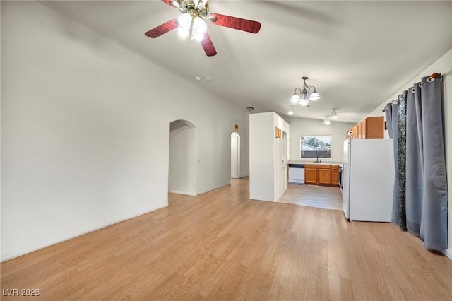 unfurnished living room with arched walkways, lofted ceiling, ceiling fan with notable chandelier, a sink, and light wood-type flooring