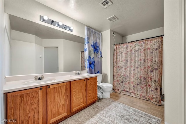 bathroom with wood finished floors, visible vents, a sink, and double vanity