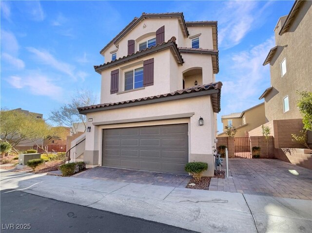 mediterranean / spanish-style house featuring an attached garage, fence, decorative driveway, and stucco siding