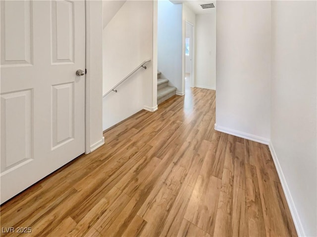 unfurnished room with light wood-style floors, visible vents, stairway, and baseboards