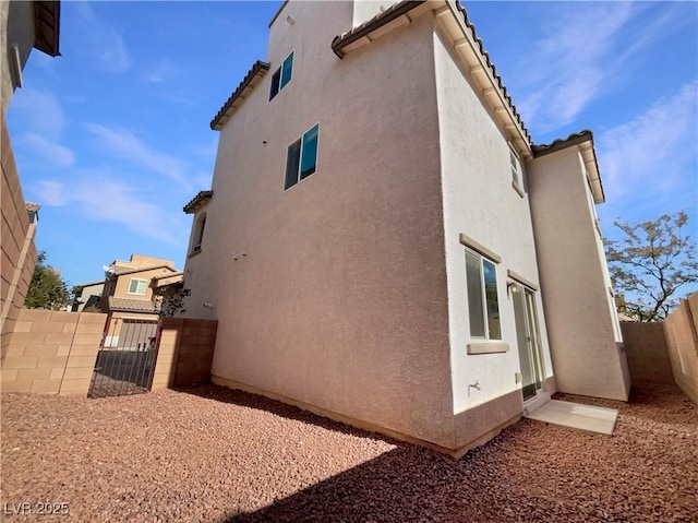 view of side of home featuring fence private yard, a gate, a tile roof, and stucco siding