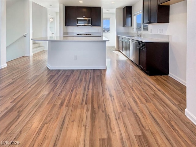 kitchen with a sink, light countertops, appliances with stainless steel finishes, dark brown cabinets, and light wood-type flooring