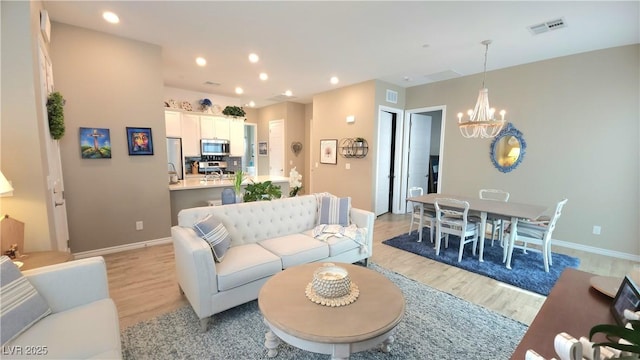 living room featuring light wood-type flooring, a notable chandelier, visible vents, and recessed lighting