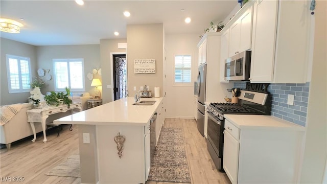 kitchen featuring tasteful backsplash, light wood-type flooring, a peninsula, appliances with stainless steel finishes, and a sink
