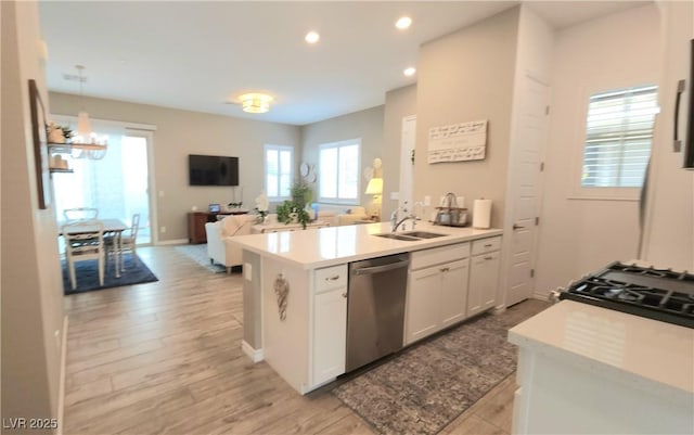 kitchen featuring open floor plan, white cabinetry, stainless steel dishwasher, light wood finished floors, and a sink