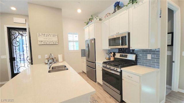 kitchen featuring white cabinets, light countertops, a sink, stainless steel appliances, and decorative backsplash