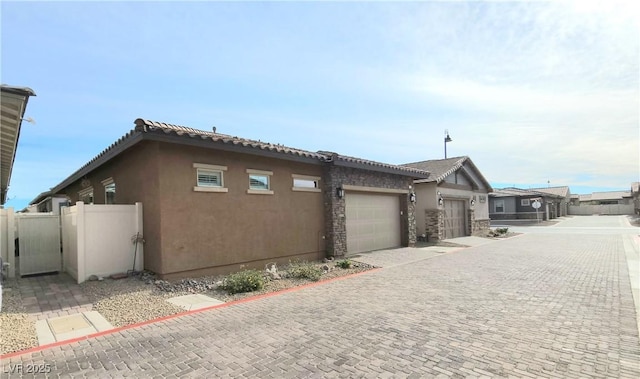 view of home's exterior featuring a garage, stucco siding, fence, and decorative driveway