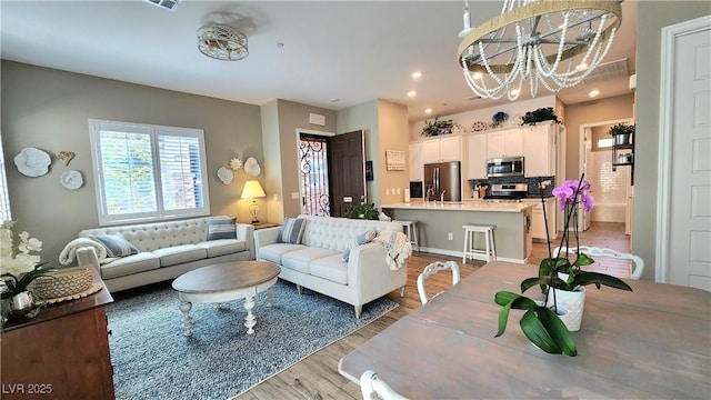 living area with visible vents, light wood-style flooring, recessed lighting, and an inviting chandelier