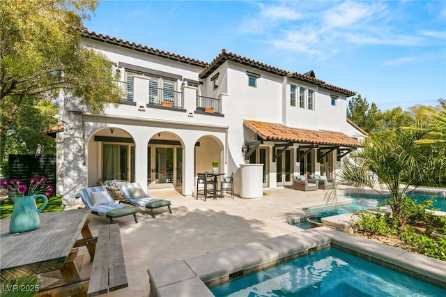 back of house with a balcony, outdoor lounge area, a pool with hot tub, a patio area, and french doors