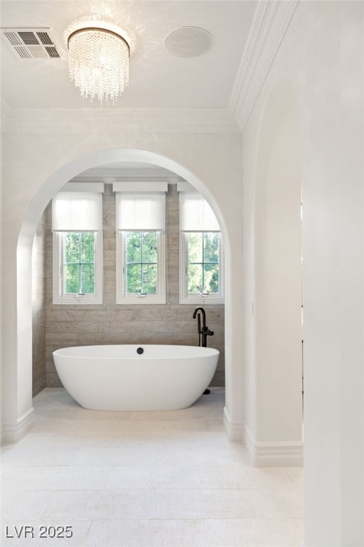 bathroom featuring a bathing tub, ornamental molding, tile walls, and an inviting chandelier