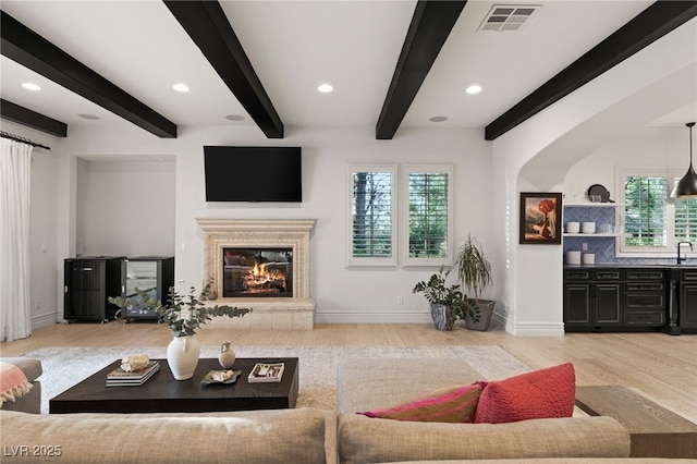 living room featuring beam ceiling, sink, and light wood-type flooring