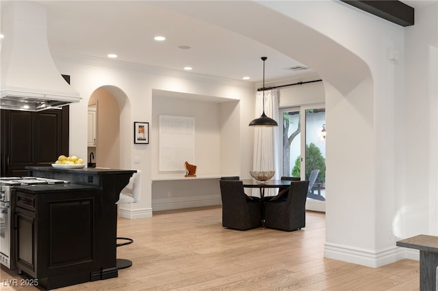 kitchen with premium range hood, decorative light fixtures, a breakfast bar area, stainless steel range, and light hardwood / wood-style flooring