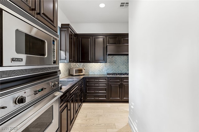 kitchen with appliances with stainless steel finishes, dark brown cabinets, decorative backsplash, and light hardwood / wood-style flooring