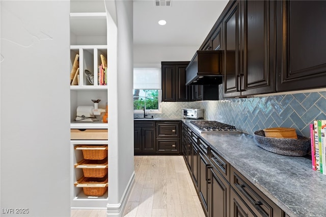 kitchen featuring tasteful backsplash, dark brown cabinetry, custom range hood, and light hardwood / wood-style flooring