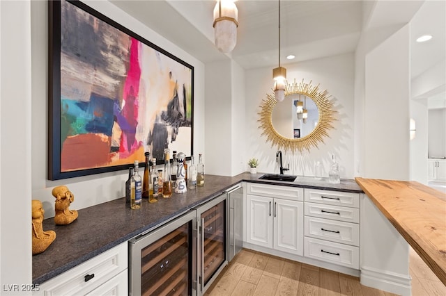 bar with sink, white cabinetry, hanging light fixtures, light wood-type flooring, and beverage cooler