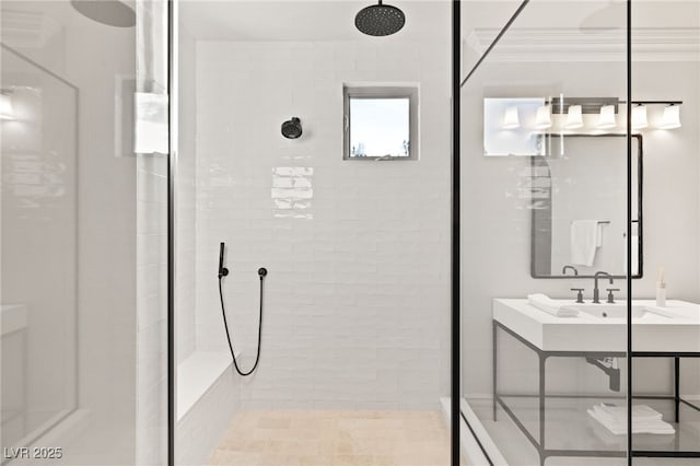 bathroom featuring a tile shower, sink, and crown molding