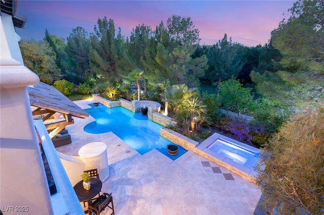 pool at dusk featuring an in ground hot tub and a patio