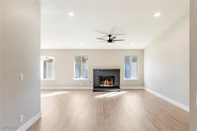 unfurnished living room with ceiling fan, a healthy amount of sunlight, a fireplace, and light hardwood / wood-style floors