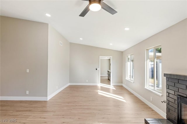 unfurnished living room with vaulted ceiling, ceiling fan, a fireplace, and light hardwood / wood-style flooring