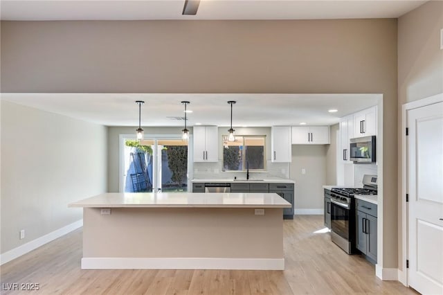 kitchen with white cabinetry, decorative light fixtures, appliances with stainless steel finishes, a kitchen island, and backsplash