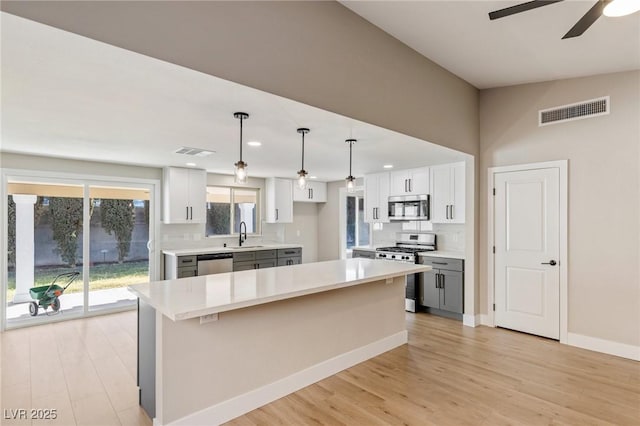 kitchen with white cabinetry, decorative light fixtures, a center island, appliances with stainless steel finishes, and backsplash