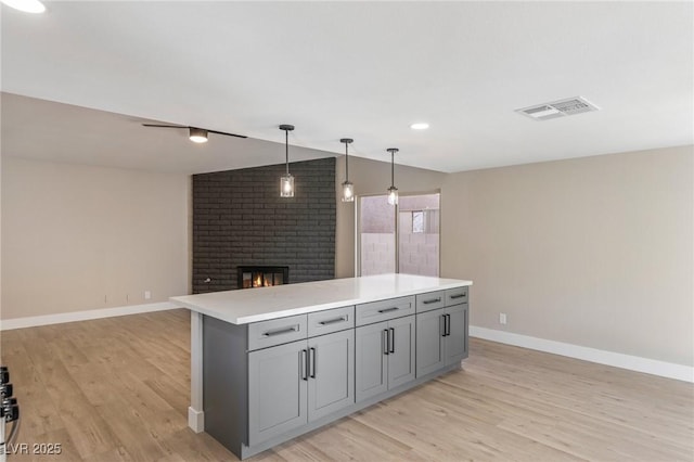 kitchen featuring hanging light fixtures, a center island, a fireplace, and gray cabinets