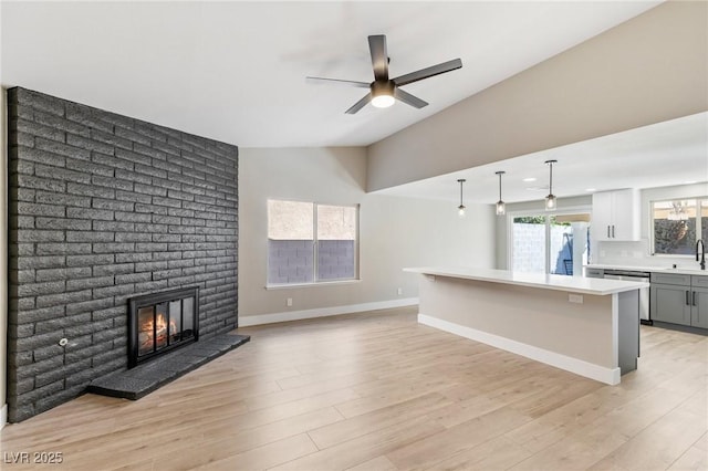 unfurnished living room with sink, vaulted ceiling, light hardwood / wood-style flooring, ceiling fan, and a fireplace