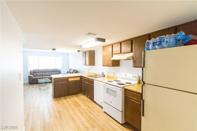 kitchen with white appliances, kitchen peninsula, sink, and light wood-type flooring