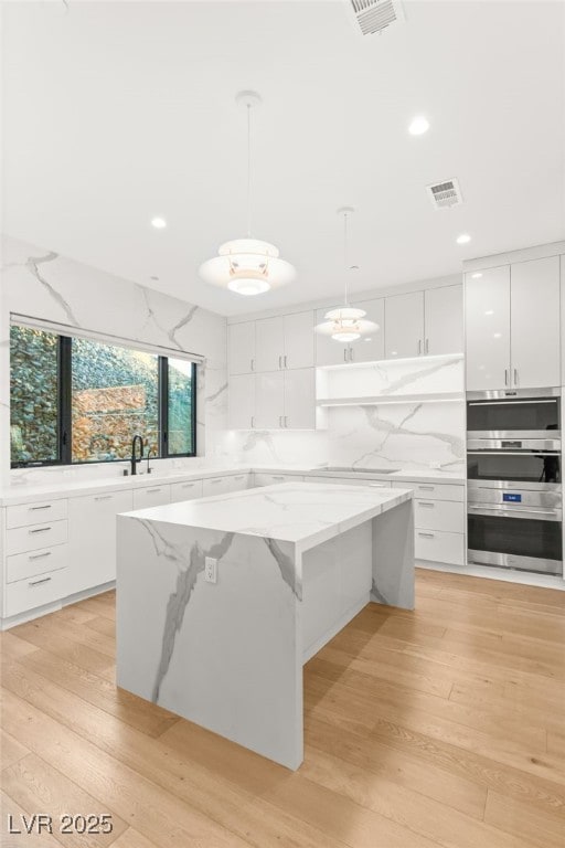 kitchen featuring hanging light fixtures, light hardwood / wood-style floors, white cabinets, a kitchen island, and stainless steel double oven