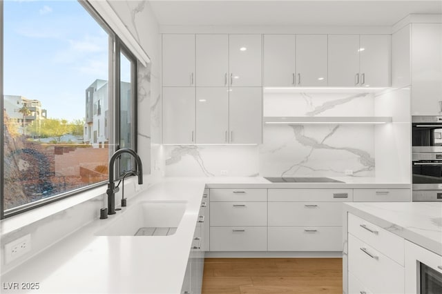 kitchen featuring white cabinetry, sink, black electric cooktop, and light wood-type flooring