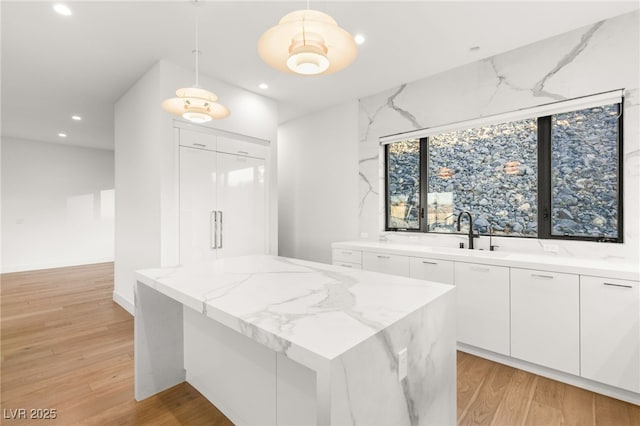 kitchen featuring pendant lighting, light stone countertops, sink, and white cabinets