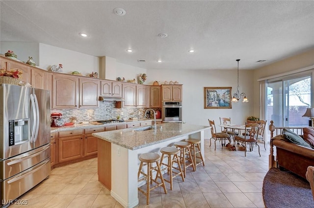 kitchen featuring sink, a kitchen island with sink, backsplash, stainless steel appliances, and decorative light fixtures