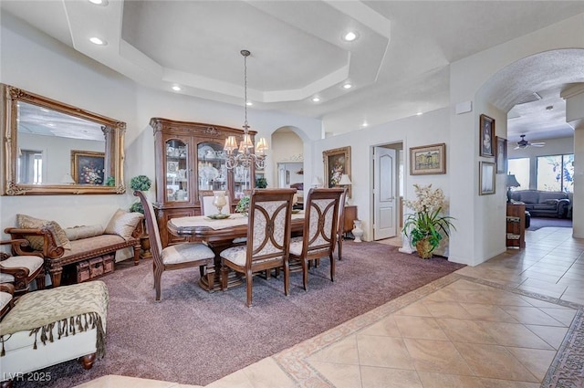 dining area with a raised ceiling, ceiling fan with notable chandelier, and light tile patterned floors