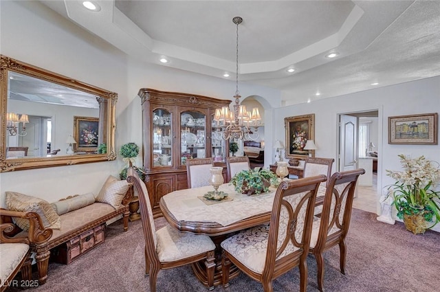 carpeted dining area with a tray ceiling and a chandelier