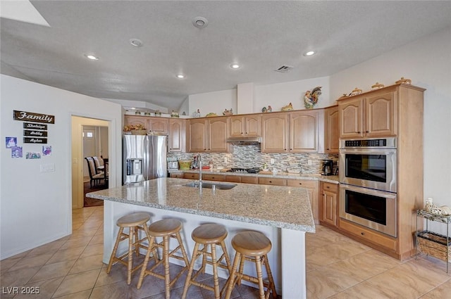 kitchen with light stone counters, stainless steel appliances, a breakfast bar, and a kitchen island with sink