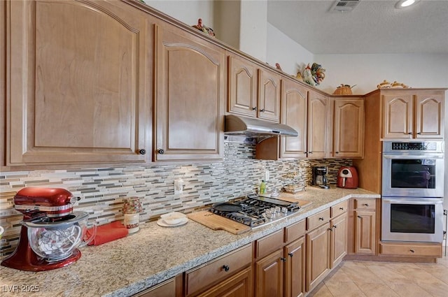 kitchen with tasteful backsplash, stainless steel appliances, light stone countertops, and light tile patterned floors