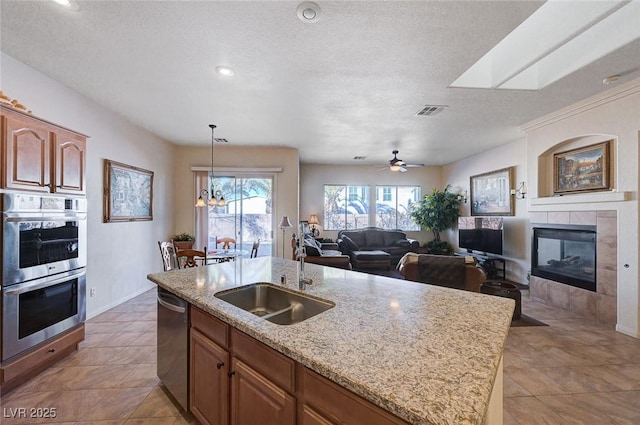 kitchen featuring an island with sink, sink, a tiled fireplace, stainless steel appliances, and a textured ceiling