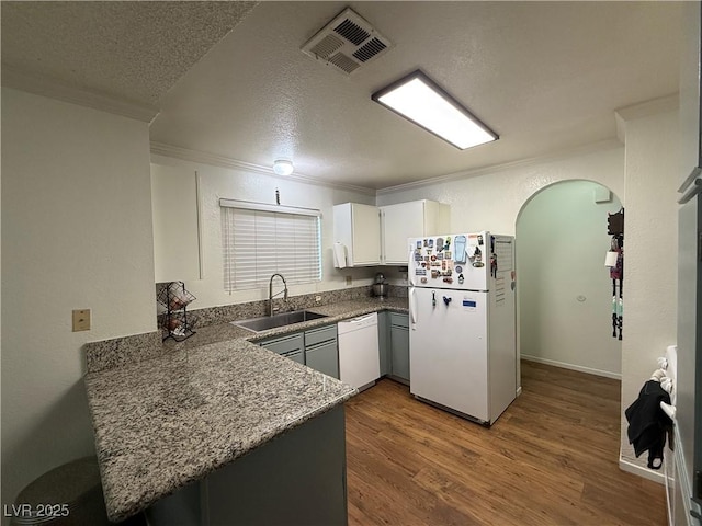 kitchen with sink, white appliances, wood-type flooring, ornamental molding, and white cabinets