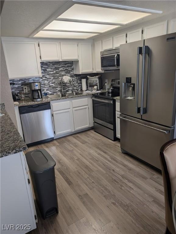 kitchen with sink, appliances with stainless steel finishes, white cabinets, dark stone counters, and light wood-type flooring