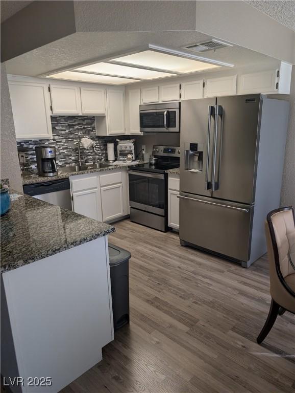 kitchen with sink, appliances with stainless steel finishes, white cabinetry, dark stone countertops, and wood-type flooring