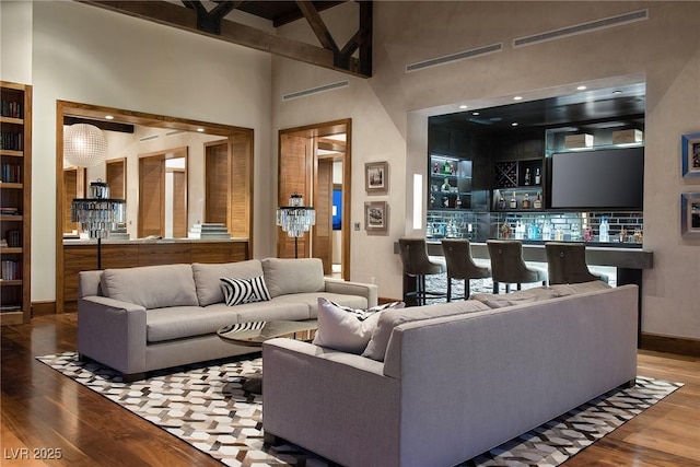 living room with wood-type flooring, a towering ceiling, and bar area