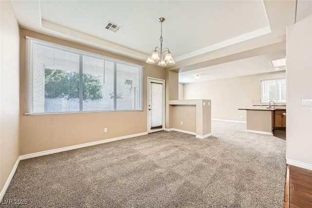 unfurnished room featuring a raised ceiling, dark carpet, and a notable chandelier